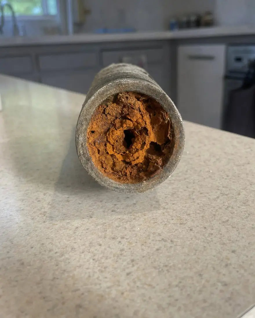 A corroded pipe full of rust and orange buildup, its opening nearly closed off, sitting on a kitchen counter